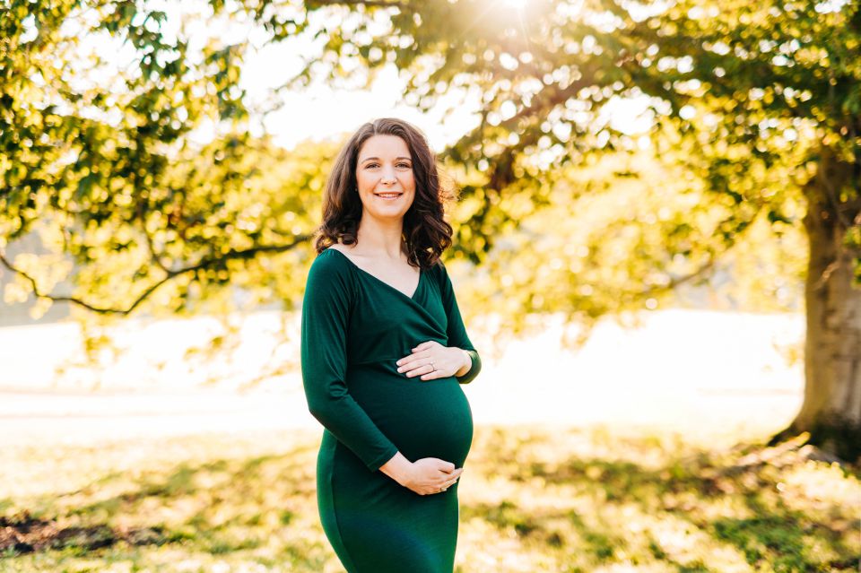 Woman in dark green dress posing for maternity portraits at Green Spring Gardens in Alexandria, VA